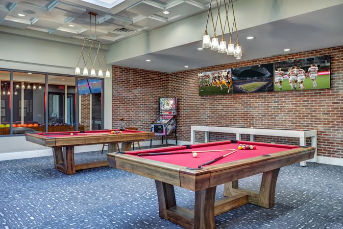 Modern entertainment room with bright red billiard tables, cozy seating, and vibrant sports-themed decor.