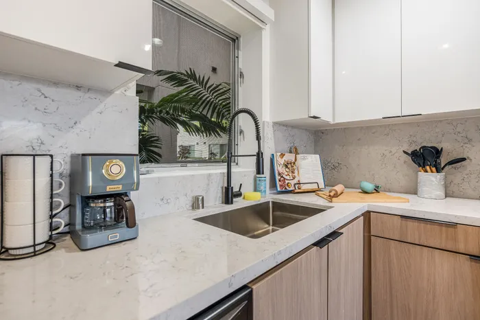 Modern kitchen with elegant marble countertops, stylish faucet, and large window view, featuring a chic coffee maker and sleek cabinetry.