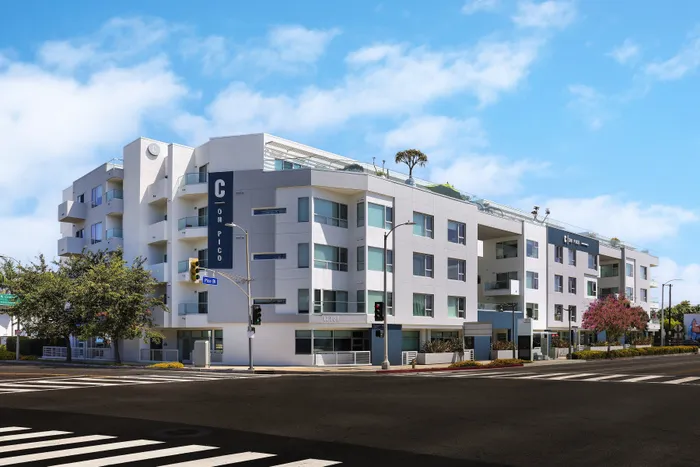 Modern apartment complex on a sunny intersection, showcasing a sleek design with spacious balconies and lush landscaping.