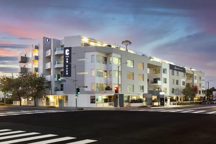 Modern apartment complex with striking architectural design, featuring spacious balconies and illuminated at dusk.