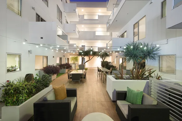 Modern apartment courtyard with elegant patio furniture, lush greenery, and ambient string lights for a serene atmosphere.