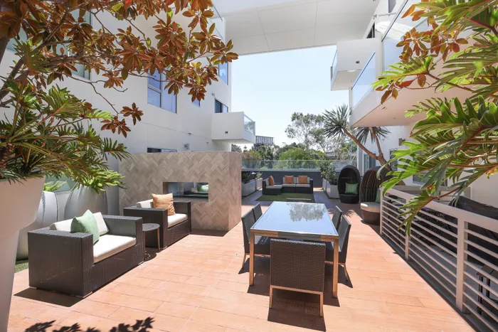 Luxurious outdoor patio featuring stylish wicker furniture, elegant dining set, and lush greenery in a modern apartment setting.