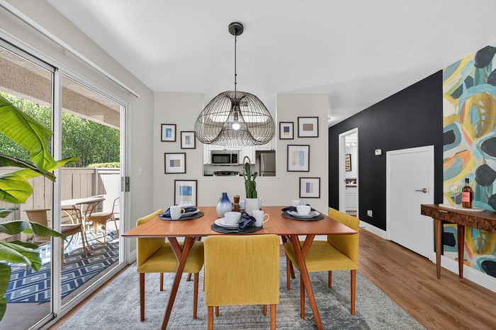 Chic dining area with vibrant yellow chairs, modern pendant lighting, and stylish artwork, opening to a serene outdoor patio.
