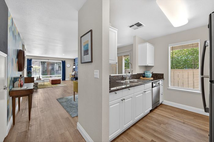 Bright and inviting living area with modern decor, connected to a sleek white kitchen featuring granite countertops and stainless steel appliances.