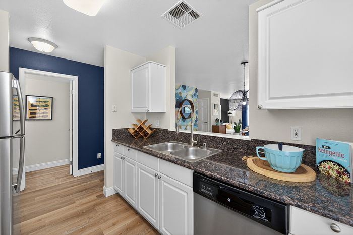 Modern kitchen with sleek countertops, wooden flooring, and stainless steel appliances connected to a stylish living area.