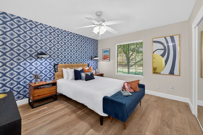 Elegant bedroom with chic geometric wallpaper, cozy queen bed, and stylish decor, inviting natural light through large window.