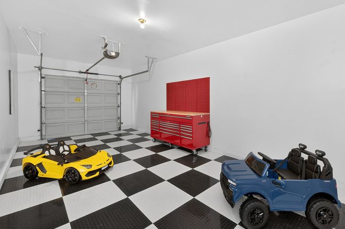 Modern garage with sleek checkered flooring, featuring vibrant yellow and blue toy cars and a bold red tool chest.