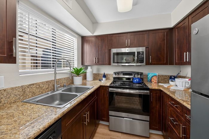 Modern kitchen with dark wood cabinetry, stainless steel appliances, and sleek granite countertops.