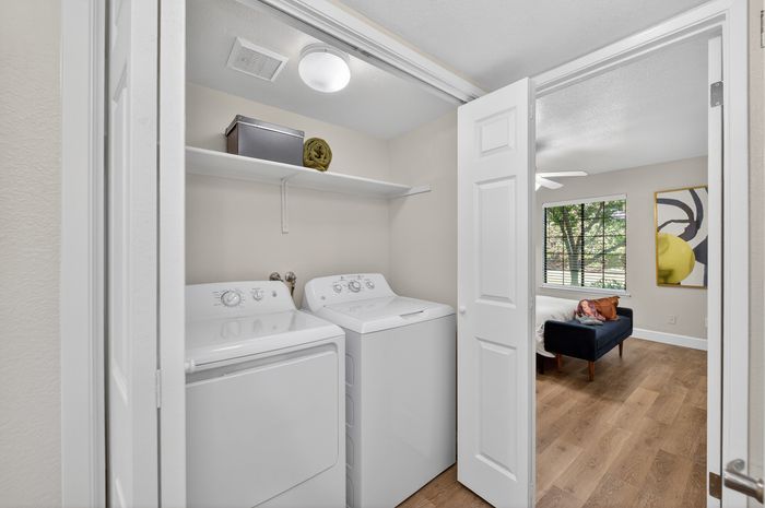 Bright apartment featuring an in-unit laundry area with modern washer and dryer, complemented by a stylish nearby living space.