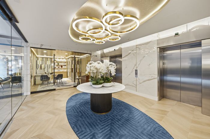 Luxurious apartment lobby with elegant marble floors and modern circular lighting, featuring a stylish seating area and vibrant orchid centerpiece.