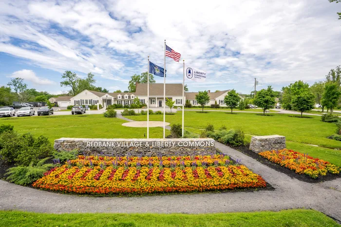 Charming entrance to Redbank Village & Liberty Commons featuring vibrant flower beds and welcoming flags.