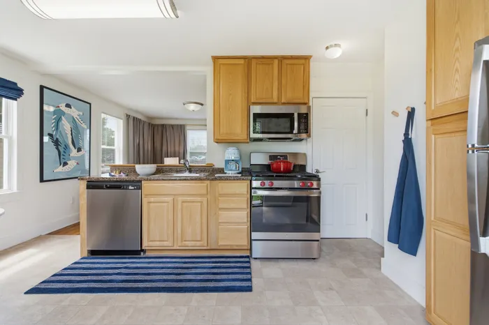 Bright, modern kitchen boasting sleek stainless steel appliances and charming wooden cabinetry, accented by an artistic wall piece and a cozy atmosphere.