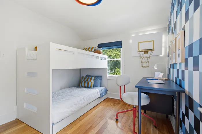 Bright children's room featuring cozy bunk beds, a colorful checkered accent wall, and a playful basketball hoop above a neat study desk.