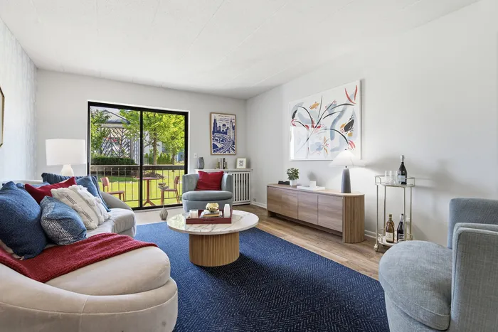 Inviting living room with chic furniture, vibrant artwork, and large window overlooking a serene green garden.