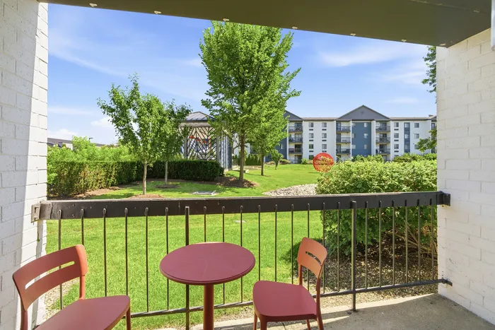 Inviting apartment balcony overlooking lush green lawns and modern apartment buildings with outdoor seating.