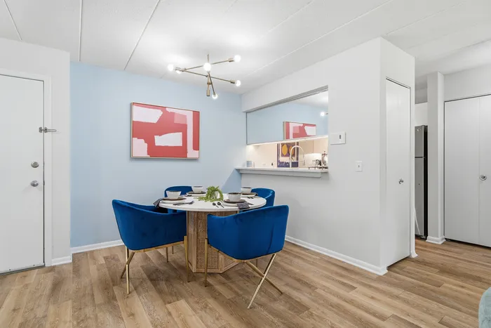 Modern dining area with stylish blue velvet chairs, chic light fixture, and sleek hardwood floors, adjacent to a cozy serving hatch to the kitchen.