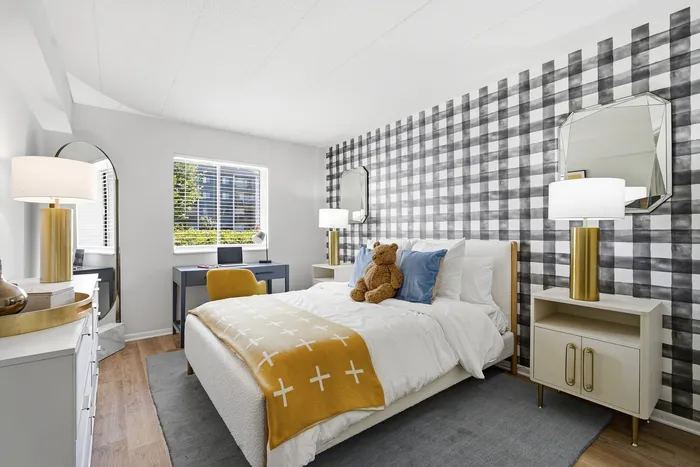 Chic bedroom with modern plaid accent wall, cozy bed with mustard throw, natural light, and elegant gold lamp accents.