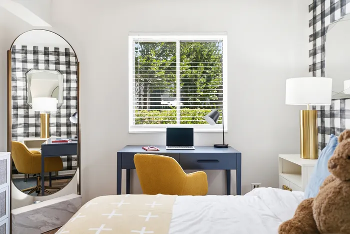 Bright and inviting bedroom featuring a stylish work desk, plush yellow chair, and large window with lush greenery view.