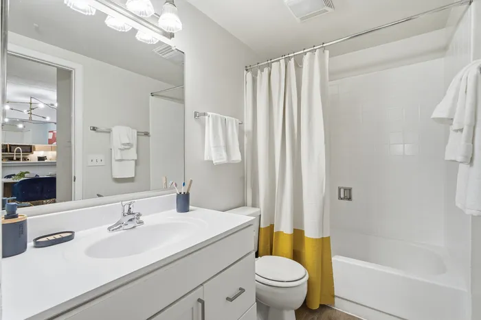 Modern bathroom with sleek white vanity, full bathtub, stylish lighting, and a vibrant yellow-accented shower curtain.