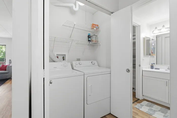 Bright apartment laundry area with in-unit washer and dryer, adjacent to a modern bathroom featuring sleek cabinetry and abundant natural light.