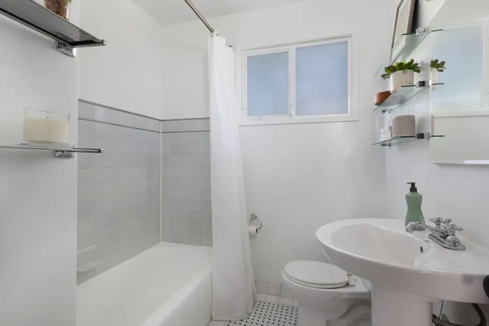 Bright, modern bathroom featuring a sleek pedestal sink, elegant white tile, and glass shelving with decorative plants.