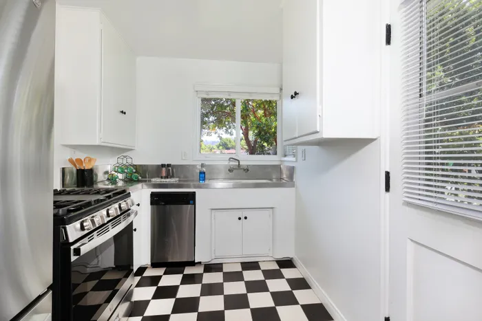 Bright and modern kitchen featuring sleek stainless steel appliances, classic black and white checkered flooring, and large windows with a scenic view.