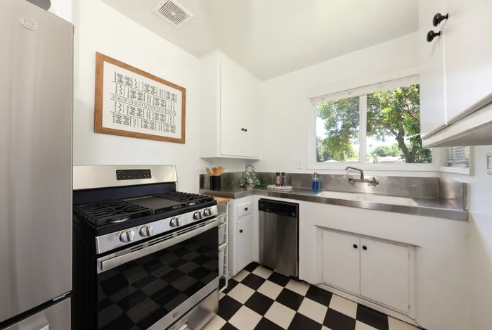 Charming kitchen with a modern stainless steel stove, elegant checkerboard floor, and large window offering abundant natural light.