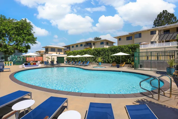 Inviting outdoor pool area with modern lounge chairs, vibrant greenery, and a serene atmosphere under a bright blue sky.
