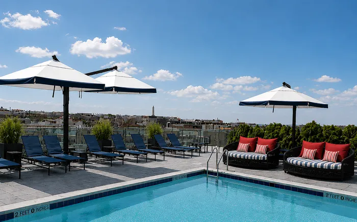 Luxurious rooftop pool area with sleek lounge chairs, stylish umbrellas, and vibrant red cushions against a stunning cityscape backdrop.