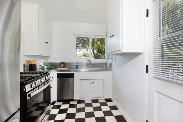 Bright and modern kitchen featuring sleek stainless steel appliances, classic black and white checkered flooring, and large windows with a scenic view.