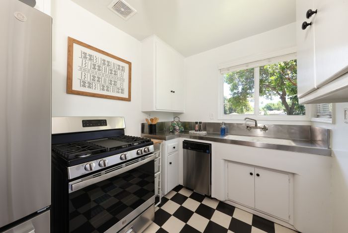 Charming kitchen with a modern stainless steel stove, elegant checkerboard floor, and large window offering abundant natural light.