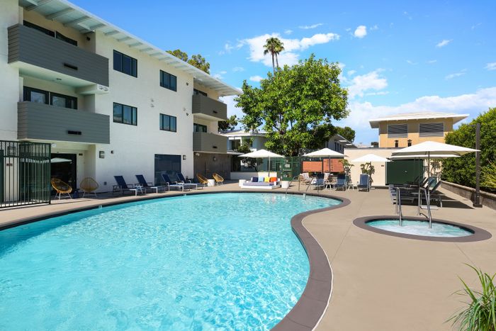 Inviting outdoor pool area with sun loungers and umbrellas, set against a modern apartment building and lush greenery.
