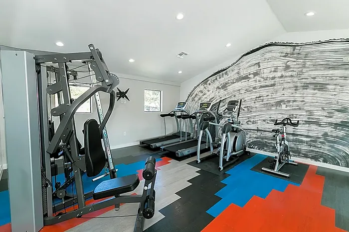 Modern fitness center featuring state-of-the-art equipment, including treadmills, stationary bike, and multi-functional weight machine, with stylish wall art and vibrant flooring.