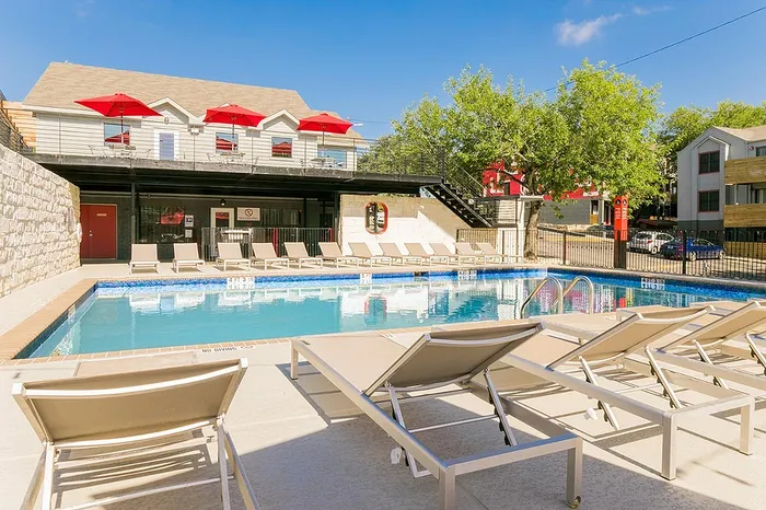 Inviting outdoor pool area with stylish lounging chairs and vibrant red umbrellas, ideal for relaxation and entertainment.