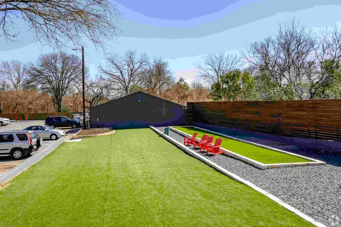 Charming outdoor space featuring a lush green lawn with vibrant red chairs, perfect for relaxation and social gatherings.
