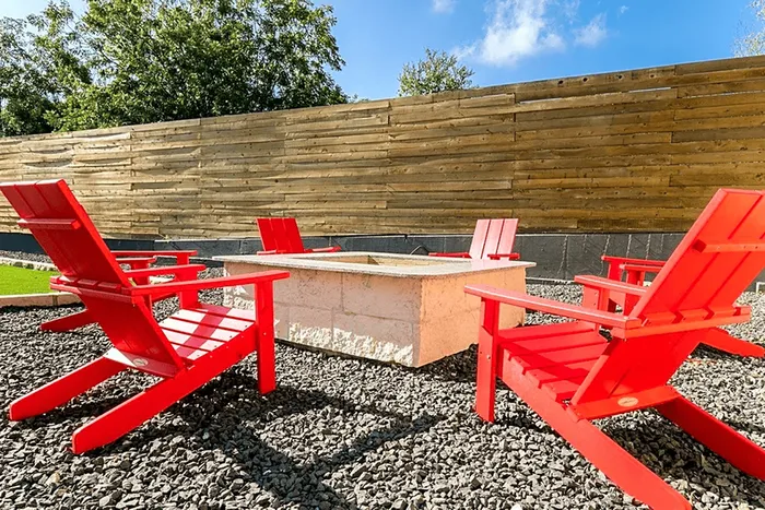 Inviting outdoor space with vibrant red Adirondack chairs surrounding a modern stone fire pit, set against a stylish wooden privacy fence.