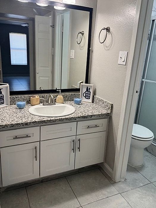 Modern bathroom with sleek granite countertops, stylish white cabinetry, and a contemporary mirror.