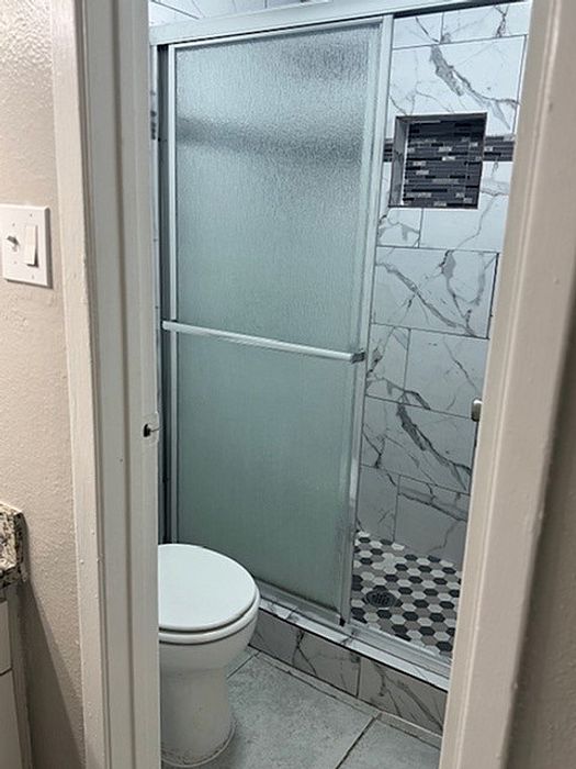 Chic bathroom with a marble-tiled shower, sleek sliding glass door, and modern fixtures.