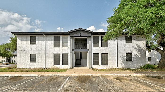 Charming two-story apartment building with a classic brick facade, nestled amid lush greenery and featuring spacious parking.