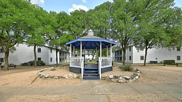 Charming courtyard with a central gazebo surrounded by lush trees and welcoming pathways, enhancing the appeal of this peaceful apartment community.