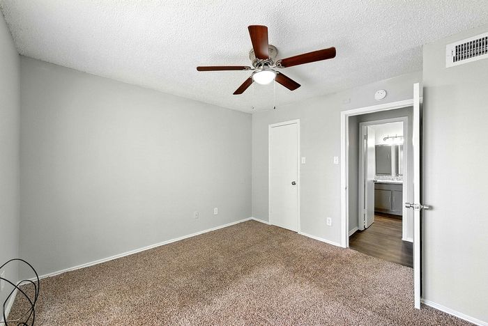 Bright and spacious bedroom featuring plush carpet, neutral walls, and a modern ceiling fan leading to a stylish en-suite bathroom.