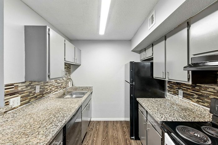 Modern kitchen featuring sleek granite countertops, stylish tiled backsplash, and black appliances, creating an elegant culinary space.