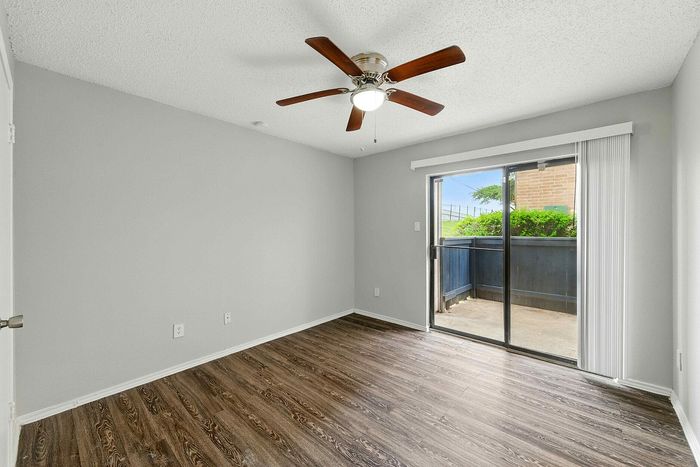 Bright, modern apartment bedroom featuring elegant wood flooring, a ceiling fan, and direct patio access through sliding glass doors.