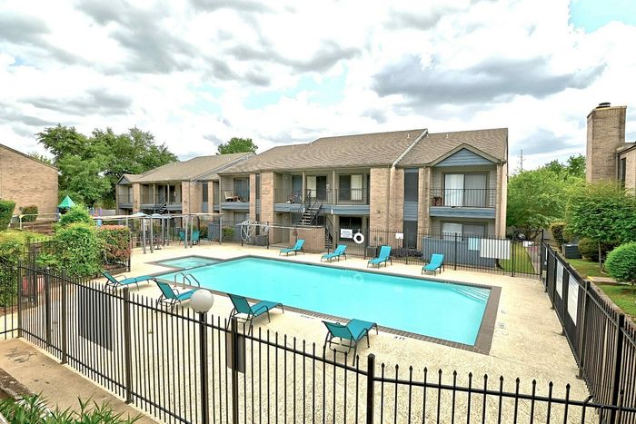 Inviting apartment complex with a sparkling swimming pool surrounded by lush greenery and modern lounging chairs.