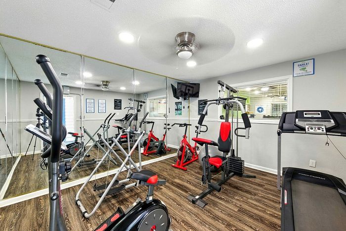 Contemporary fitness room with mirrored walls and modern gym equipment, including a treadmill, bikes, and weight machine.