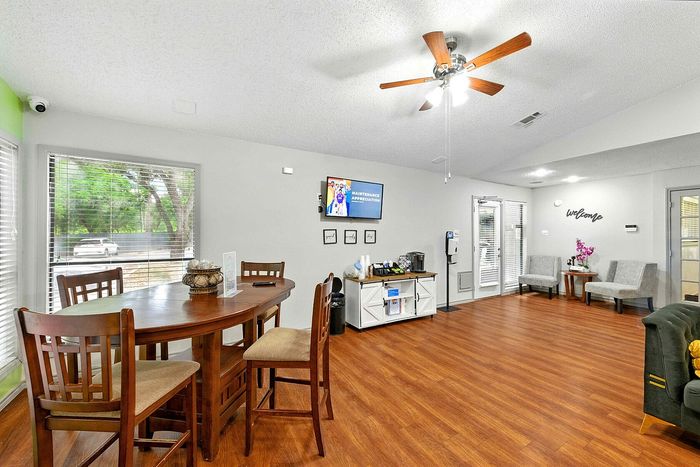 Inviting community room with modern decor, featuring a cozy seating area, wooden dining table, and large windows for natural light.