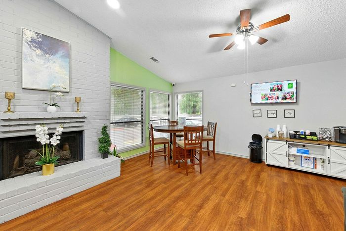 Inviting living space with bright decor, featuring a cozy brick fireplace, modern ceiling fan, and elegant dining area with hardwood floors.