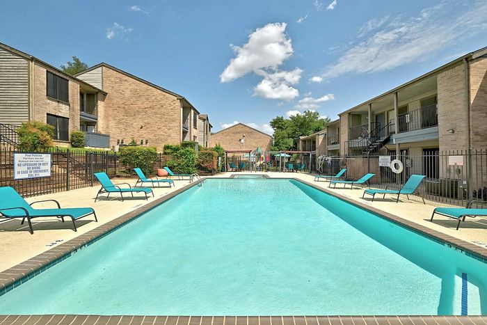 Inviting apartment complex with a sparkling swimming pool, surrounded by elegant lounge chairs under a bright blue sky, perfect for relaxation and leisure.