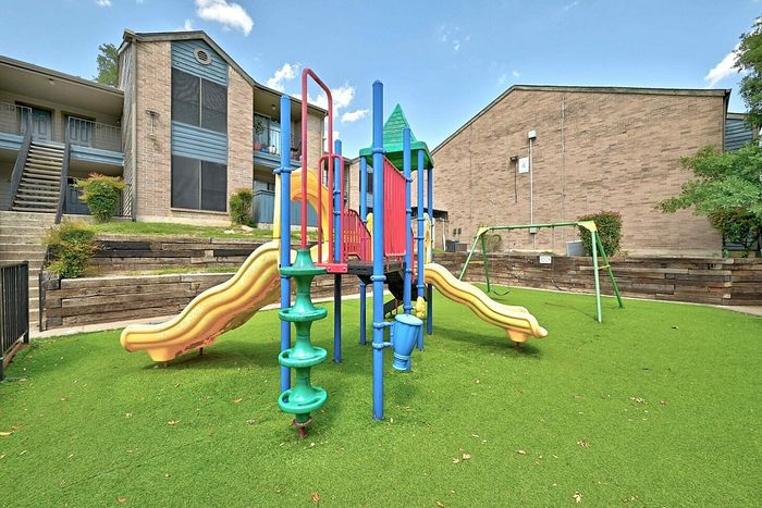 Charming apartment complex featuring a vibrant playground with colorful slides and swings, surrounded by lush greenery.