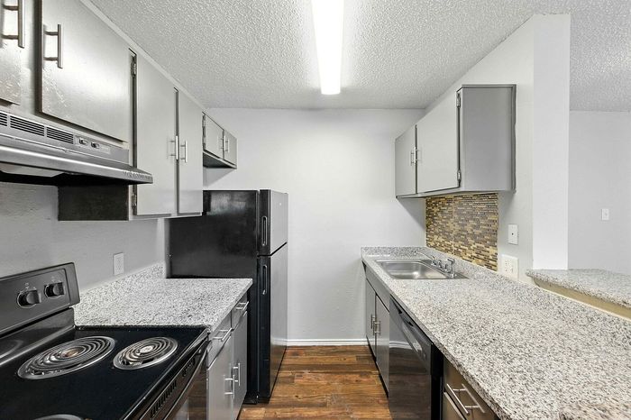 Modern kitchen with sleek gray cabinets, granite countertops, and stainless steel appliances, featuring elegant wooden flooring and a stylish backsplash.